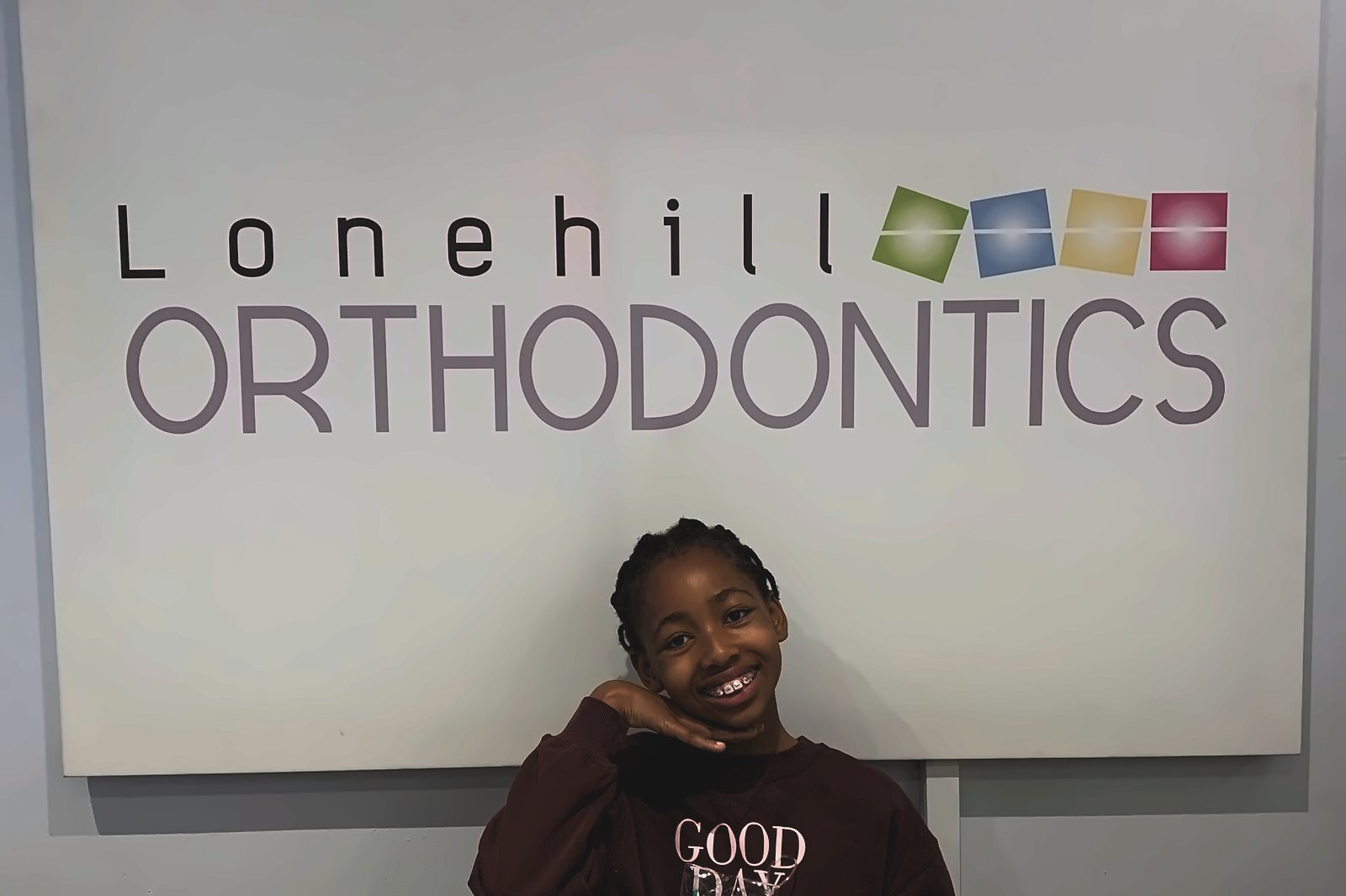 Young patient smiling with coloured metal braces at the Lonehill Orthodontics practice sign